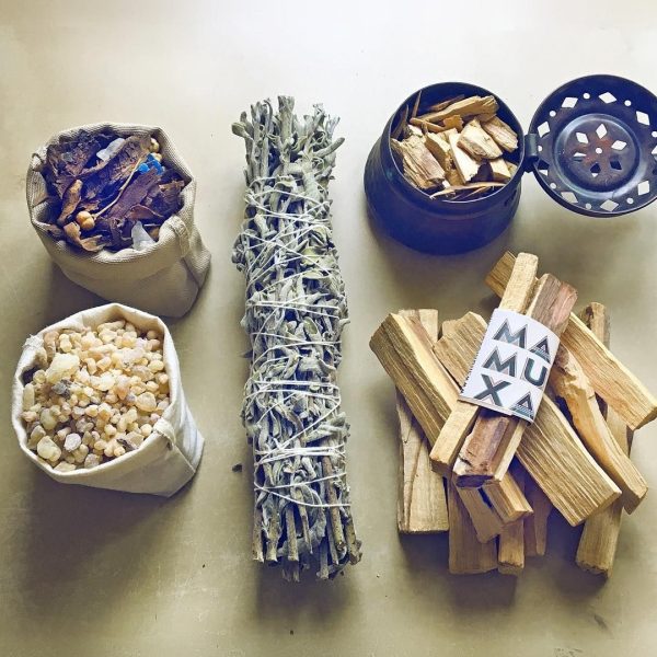 Bakhoor and frankincense resin in cotton pouches, a white sage bundle, palo santo sticks and a copper incense burner